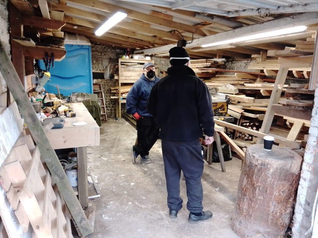 Inside the wood store, two men standing discussing the finer points of wood cutting.